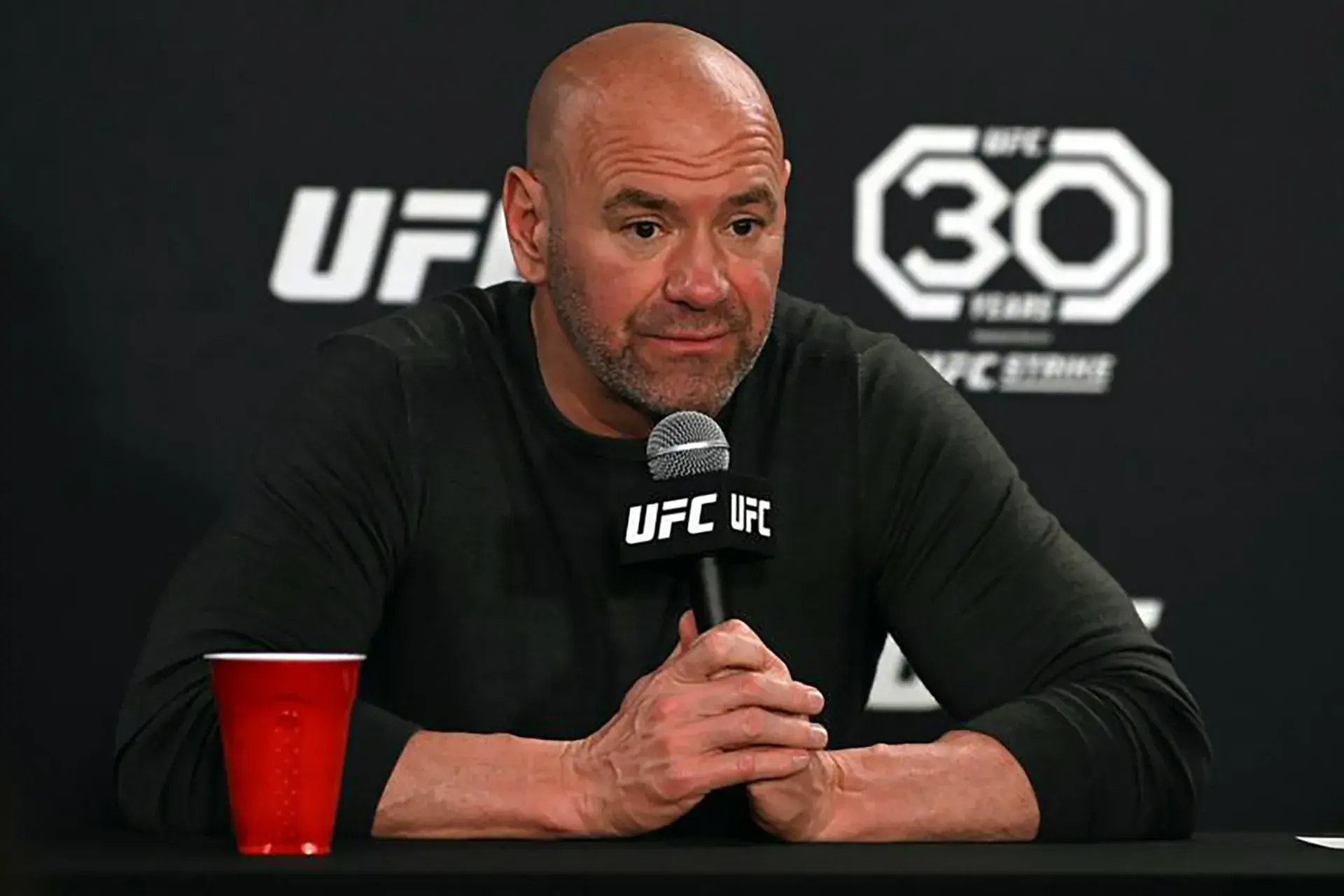 Dana White sits holding a microphone at a UFC Press Conference.
