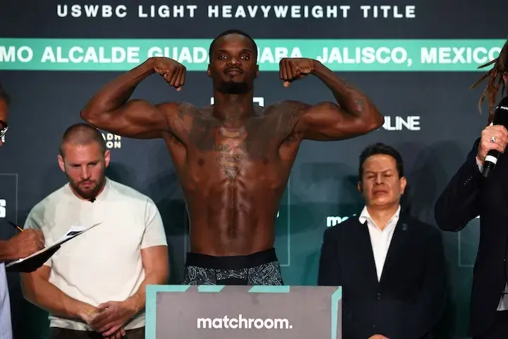 Khalil Coe stands on a scale in his underwear, with his arms up to flex his biceps muscles.