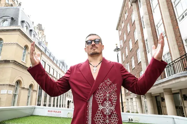 Oleksandr Usyk stands between buildings with his arms raised on July 15, 2025