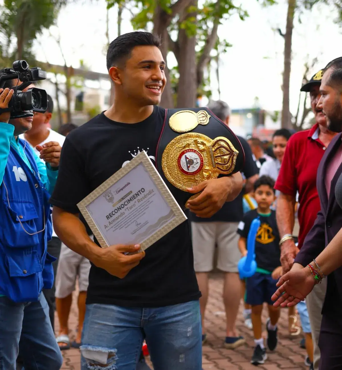 Jose Armando Resendiz holds a plaque in his right hand and a world title belt draped over his left shoulder at a parade to celebrate his victory over Caleb Plant in 2025.