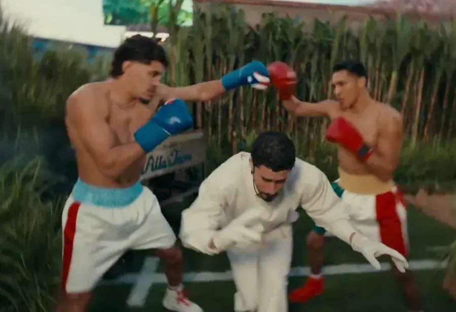 Xander Zayas and Emiliano Vargas punch each other's gloves as Bad Bunny walks underneath.