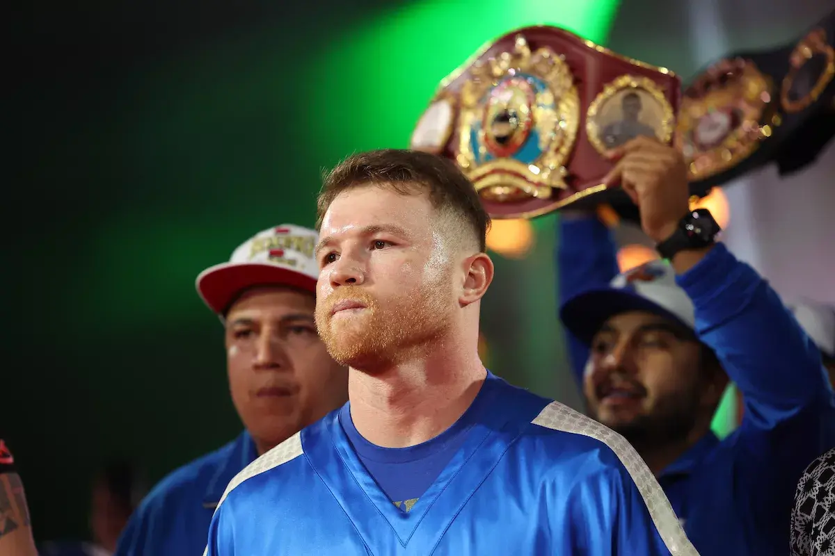 Canelo Alvarez walks to the ring wearing a blue outfit while two members of his team stand behind him, one holding a championship belt in the air, ahead of Canelo's fight with William Scull on May 3, 2025.